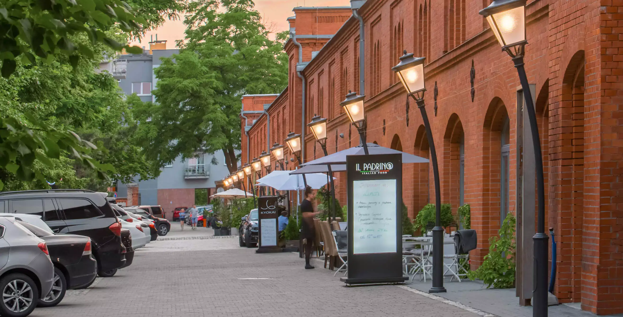 Ceglana fasada Starych Koszar wieczorem — restauracje i latarnie wzdłuż ulicy