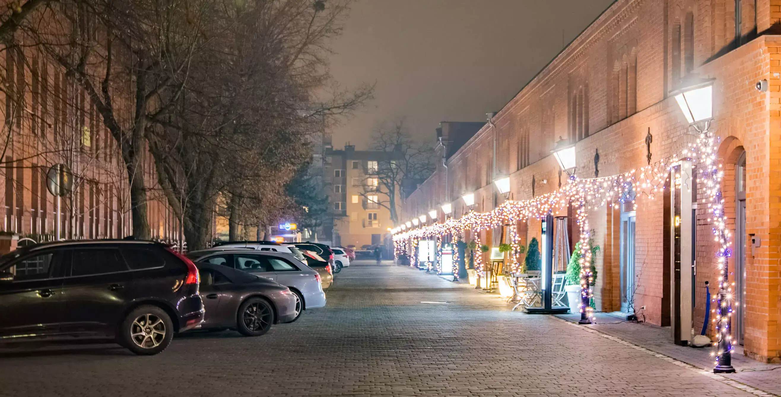 Stare Koszary wieczorem — zapalone latarnie i świąteczne światełka wzdłuż ceglanej elewacji
